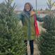 Alice in a green coat standing in between two Christmas trees