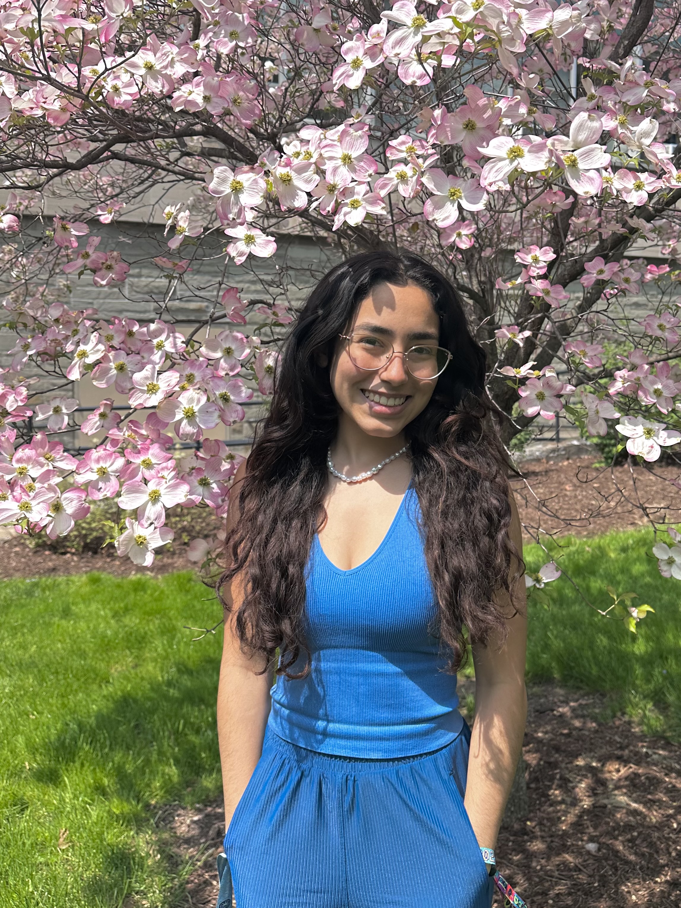 Silene with long hair down, blue top smiling under a cherry blossom tree