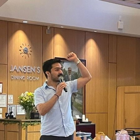 Farhad speaking into a microphone with one arm up