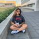 Aalayna, Cornell shirt, sitting cross legged on the ground, outside, smiling