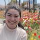 Naomi with her hair pulled back, smiling, outside, in front of tulips